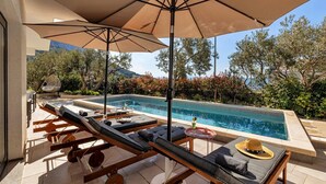 A poolside area with lounge chairs, a table, and umbrellas. - Villa Festina Lente in Makarska, heated pool (Makarska)