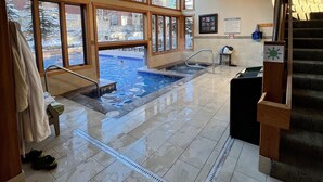 Un área de piscina interior amplia con ventanas grandes, una escalera y vistas al exterior.