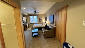 Habitación de hotel compacta con kitchenette, una cama, un sofá y un ventilador de techo.