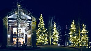 Un edificio con fachada de piedra y un nivel superior de madera, rodeado de árboles decorados con luces.