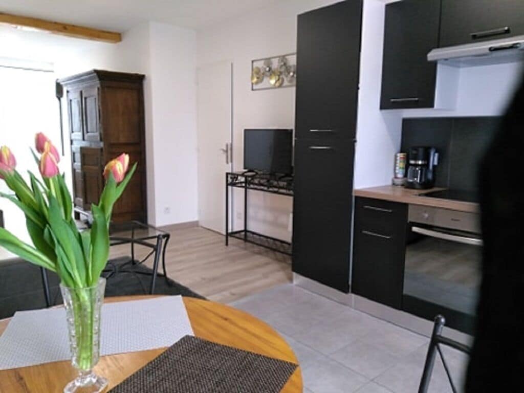 A modern kitchen with black cabinets, a gas stove, and a coffee machine. There is a dining table with a vase of flowers.