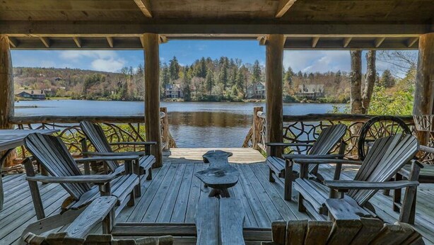 Puinen terassi, jossa on Adirondack-tyyliset tuolit ja pöytä, ja josta avautuu näkymä järvelle, jonka taustalla näkyy taloja.