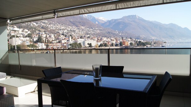 Ein Balkon mit Tisch und Stühlen, mit Blick auf eine Stadtlandschaft und dahinter Berge.
