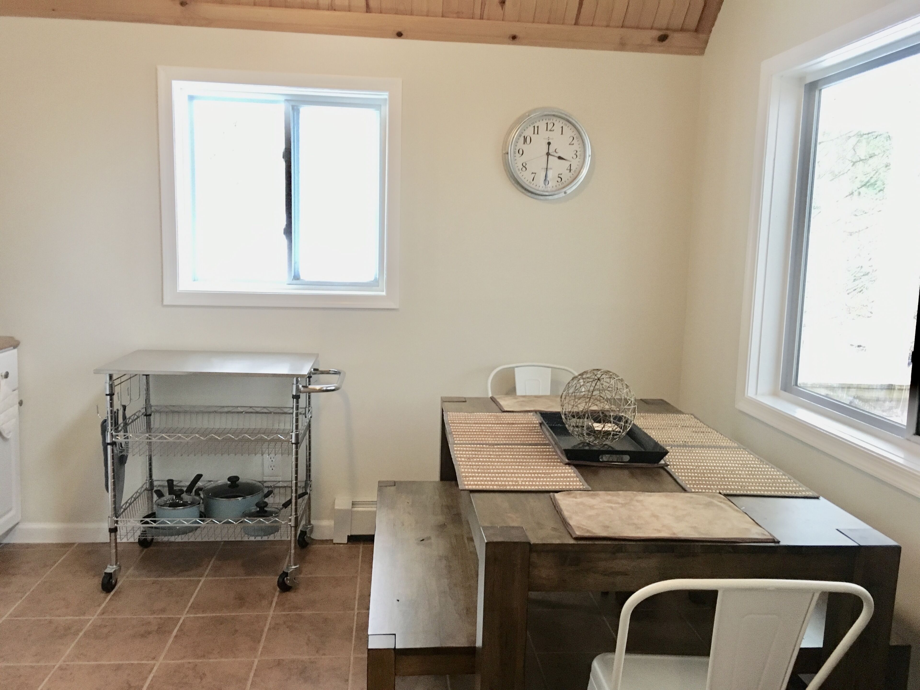 A kitchen with a dining table, a clock, and a window.