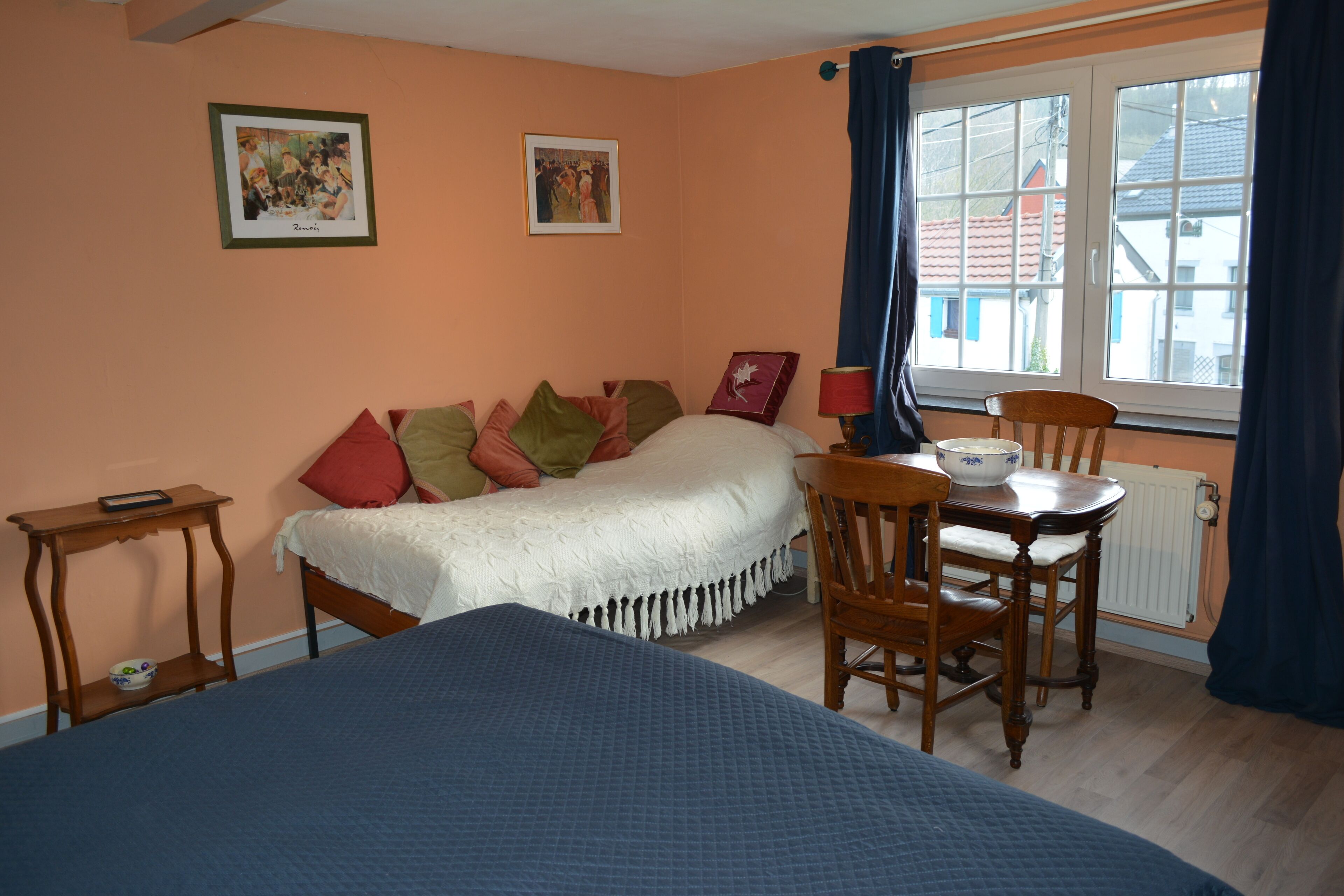A bedroom with a bed, a chair, a table, and a window with curtains.