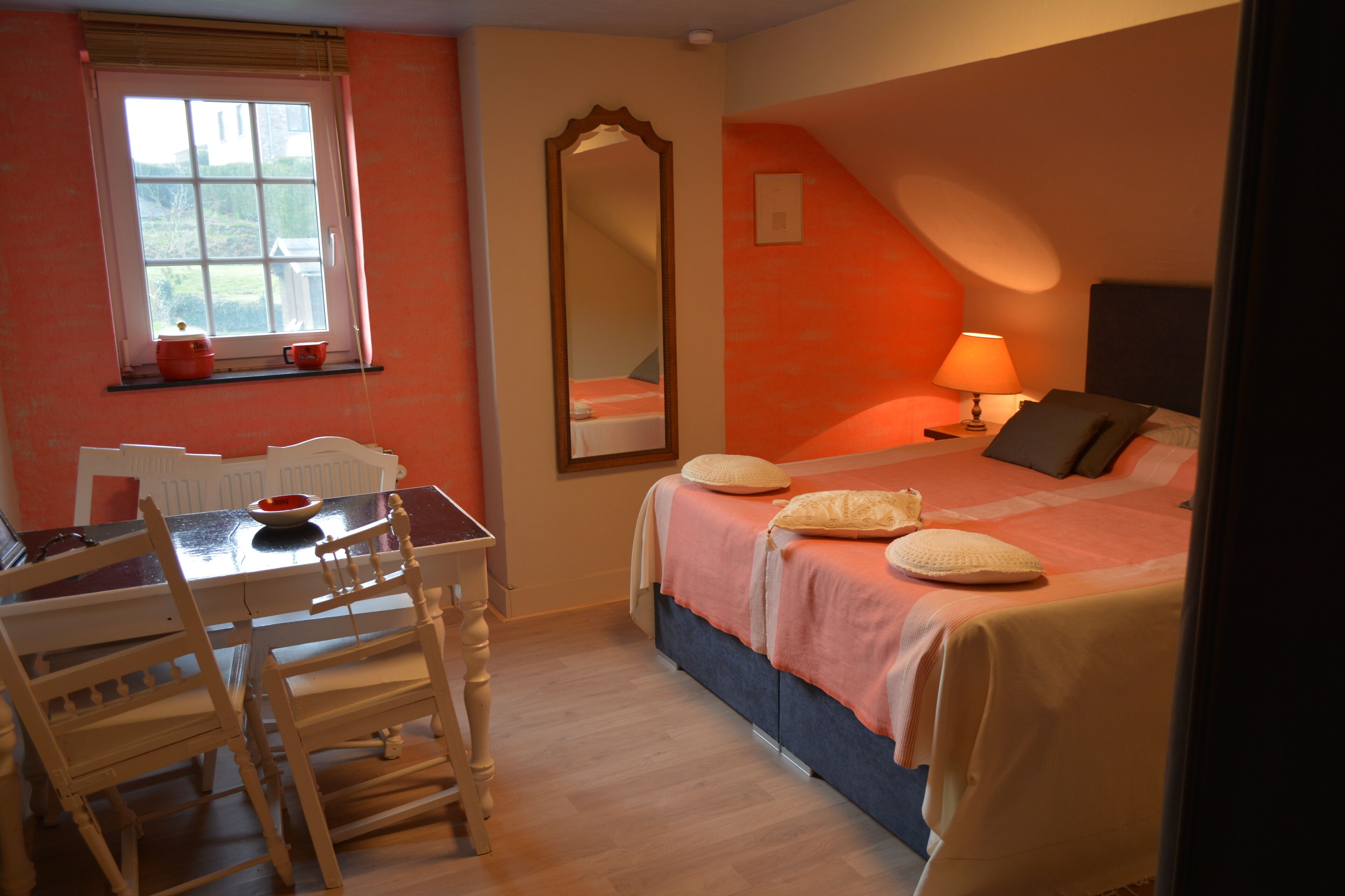 A bedroom with a bed, bedside table, lamp, and a window with a view.