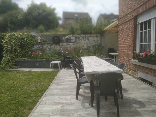 Un patio con una mesa larga y sillas, rodeado de un muro de ladrillo y follaje.