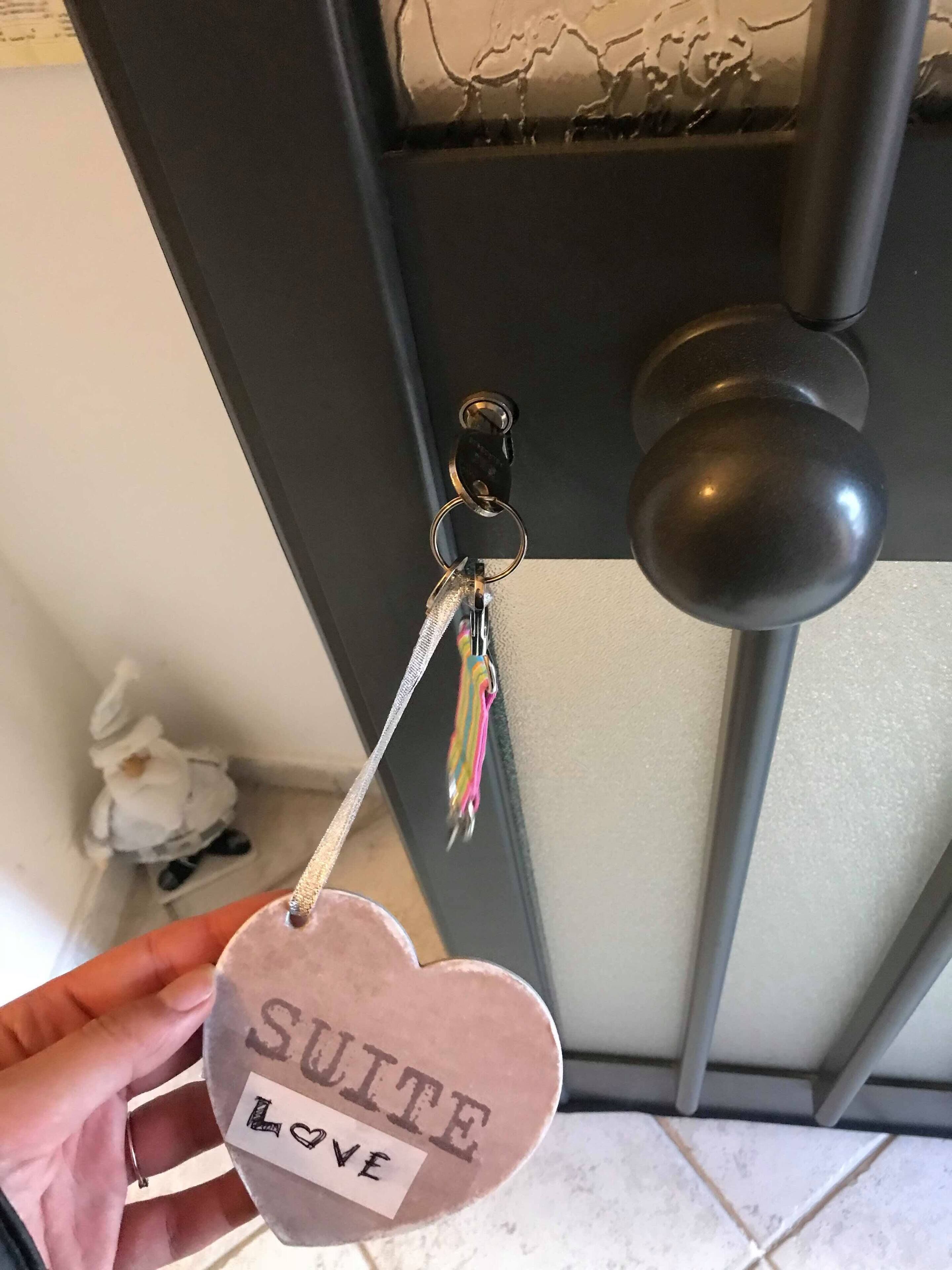 Een hand die een hartvormige sleutelhanger vasthoudt, met de tekst 'SUITE LOVE' en een sleutel eraan.