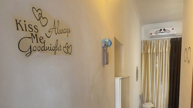 Un couloir avec une inscription sur le mur indiquant « Embrasse-moi avant de dormir », un luminaire, une porte avec un rideau et un sol carrelé.