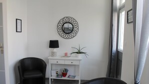 Un salon moderne avec une console blanche, un fauteuil noir, un canapé noir, un miroir décoratif et une plante en pot.