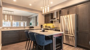 Een moderne keuken met donker houten kastjes, roestvrijstalen apparatuur en een centraal kookeiland met barstoelen.