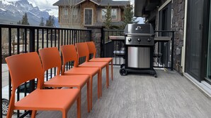 Een balkon met oranje stoelen, een barbecue en uitzicht op bergen.