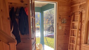 L’intérieur d’un chalet en bois, avec un chien à l’entrée, un tapis rouge à motifs et une échelle en bois.