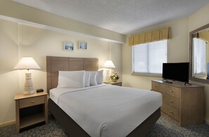 Habitación de hotel con una cama grande, dos mesitas de noche con lámparas, un aparador, un televisor y una ventana con persianas.