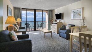 A hotel room with a balcony, a TV, a dining area, and a sofa.