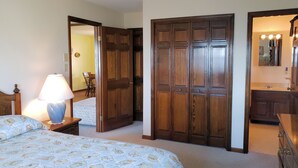 Un dormitorio con cama, mesita de noche con lámpara, armario y cómoda con espejo.