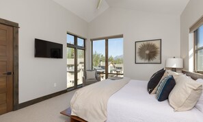 Camera da letto con un letto grande, una TV a parete, una finestra con vista su edifici e alberi, e una ventola a soffitto.