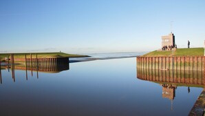 Un rivage paisible avec une jetée en bois, une petite construction en briques et une zone herbeuse.