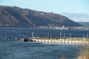 Vista del lago con un muelle que se adentra en el agua, rodeado de colinas y un pequeño pueblo al fondo.