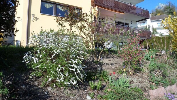 Un edificio moderno de dos pisos con un balcón y un jardín delantero.