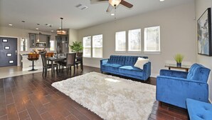 A spacious living room with a blue sofa, a white shag rug, and a ceiling fan. - RIVERWALK/ALAMODOME TOWNHOME - WITH HOT TUB & Wood Fire Pit!1 MILE TO RIVERWALK  (San Antonio)