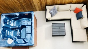 A hot tub with control knobs, a beige sofa with patterned cushions, and a small wooden table. - RIVERWALK/ALAMODOME TOWNHOME - WITH HOT TUB & Wood Fire Pit!1 MILE TO RIVERWALK  (San Antonio)