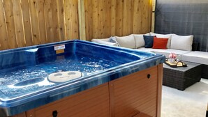 A hot tub with a wooden deck and a white couch with pillows. - RIVERWALK/ALAMODOME TOWNHOME - WITH HOT TUB & Wood Fire Pit!1 MILE TO RIVERWALK  (San Antonio)