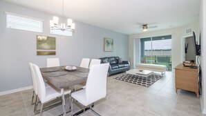 A modern dining area with a wooden table and white chairs, a blue leather sofa, and a view of the outdoors through large windows.