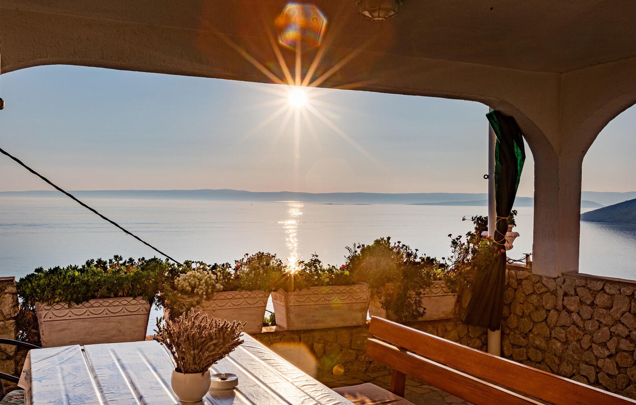 Eine Terrasse mit Meerblick, ein Tisch mit Blumen und eine Bank.