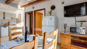 Uma cozinha compacta com geladeira, micro-ondas e um espaço de refeições com cadeiras de madeira e uma mesa posta para dois.