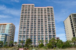 Un hôtel à plusieurs étages, doté d’une façade uniforme, de balcons et d’une enseigne indiquant qu’il s’agit d’un complexe hôtelier en bord de mer.