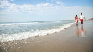 Une scène de plage où l’on voit deux personnes se promener le long du rivage.