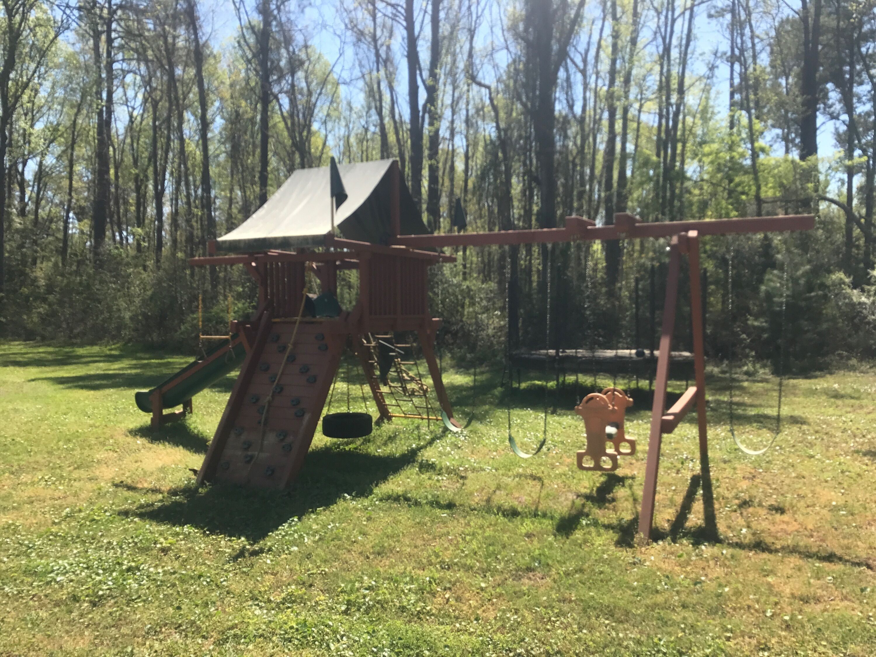 A playground with a slide and swings in a grassy area surrounded by trees.