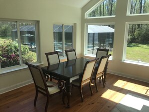 A dining room with a large table and six chairs, large windows with views of a backyard and neighboring houses. - Luxury Estate Living on five acres with a pool minutes from Downtown Beaufort (Beaufort)