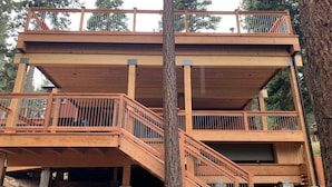 A multi-level wooden deck structure with railings and stairs, surrounded by trees.