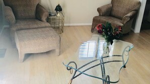 Una sala de estar con dos sillones, una mesa de centro de vidrio y una lámpara.