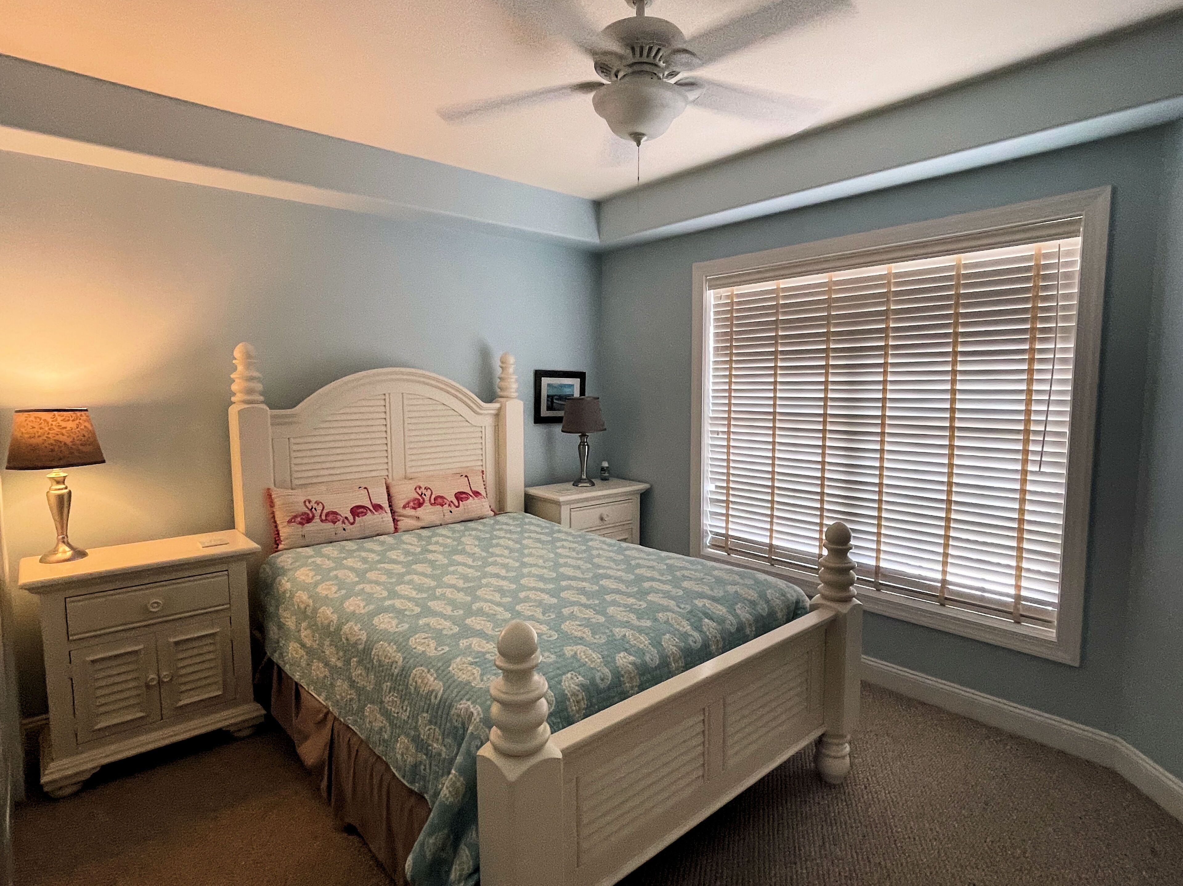 A bedroom with a bed, nightstands, a ceiling fan, and a window with blinds.