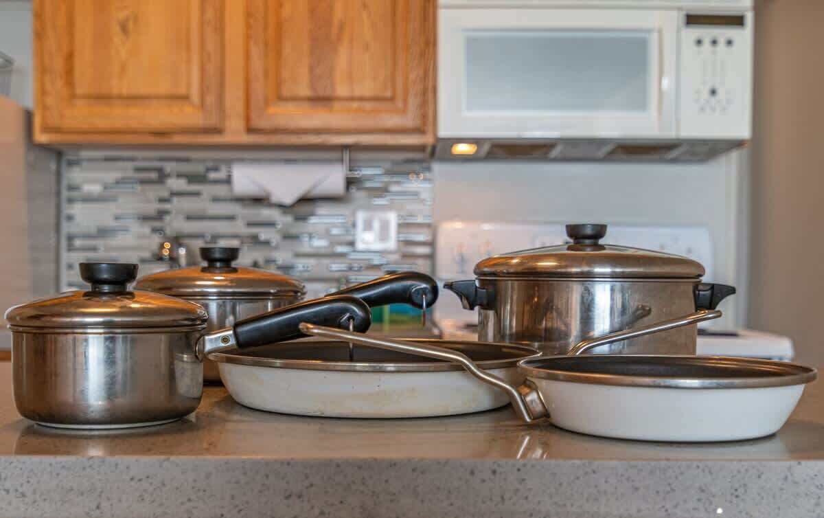 A kitchen with stainless steel cookware, a microwave, and wooden cabinets.