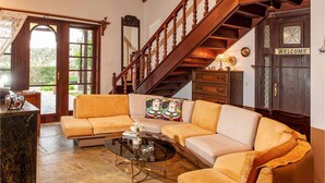 Un salon avec un escalier en bois, un ensemble de canapés, une table basse en verre et une pancarte « BIENVENUE » sur la porte.