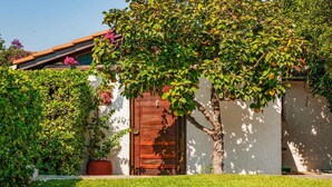 Un bâtiment rustique avec une porte en bois, entouré d’une végétation luxuriante et d’une pelouse bien entretenue.