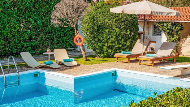 Une piscine entourée de verdure et d’un petit jardin, avec des chaises longues et des parasols à proximité.
