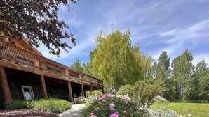 A pathway lined with pink peonies and white daisies, leading to a building with a wooden deck and stone walls. - Welcome to our Mountain Family Cabin near Lava Hot Springs!  (Bancroft)