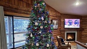 A cozy living room with a large Christmas tree, wooden walls, a fireplace, and a television. - Welcome to our Mountain Family Cabin near Lava Hot Springs!  (Bancroft)