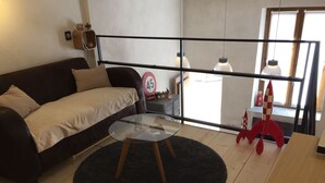 A modern living room with a sofa, a glass coffee table, a black rug, and a red rocket decoration. - "Gîte de la Fount" furnished with tourism 4 stars (Briançonnet)