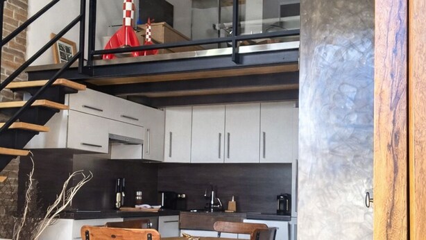 A modern kitchen with a wooden dining table and chairs, a staircase with a glass railing, and pendant lights. - "Gîte de la Fount" furnished with tourism 4 stars (Briançonnet)