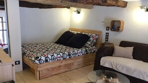 A cozy bedroom with a wooden bed, a glass coffee table, a sofa, and a small wooden cabinet. - "Gîte de la Fount" furnished with tourism 4 stars (Briançonnet)