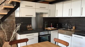 A modern kitchen with white cabinets, a black countertop, and a wooden dining table. - "Gîte de la Fount" furnished with tourism 4 stars (Briançonnet)