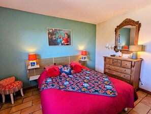 A bedroom with a bed, two bedside lamps, a dresser, a mirror, and a wall-mounted picture.