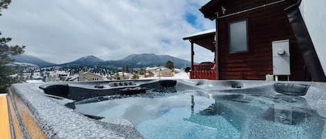 Una vasca idromassaggio con vista sulle montagne, una baita di legno e un paesaggio innevato.