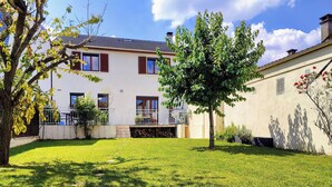 Een tweelaags huis met een verzorgd gazon, een boom in de voortuin en een balkon met een balustrade.